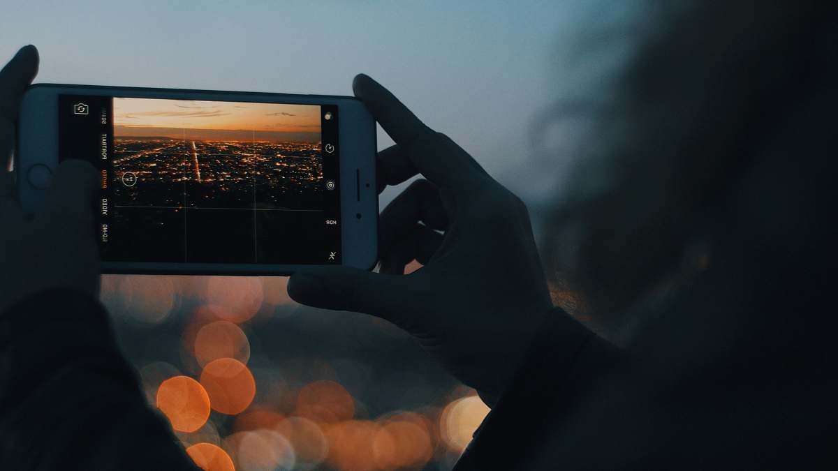 picture person capturing photo of city using iPhone during orange sunset iphone